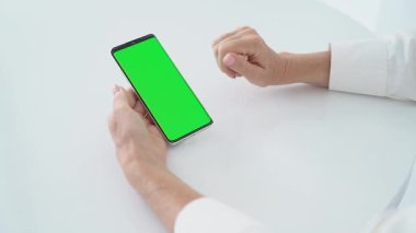 Beyaz Masa 'da Yeşil Ekran Kromakey, Dokunmatik Ekran, Mobil Teknoloji Konsepti, Dijital Tecrübe, Çevrimiçi Navigasyon, Uygulama Arayüz Tasarımı ile Kadın Elleri Akıllı Telefon.