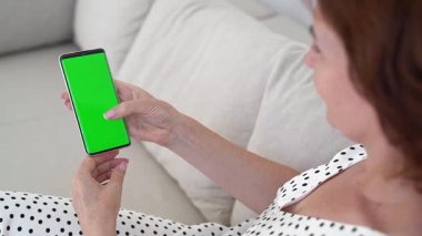 Kanepede uzanan esmer kadın, yeşil ekran gösteren akıllı telefon, ev içi titreşimler, dijital etkileşim, kablosuz iletişim, çağdaş yaşam tarzı, rahat ve bağlı.