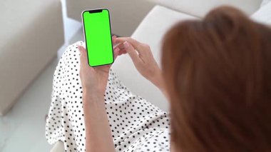 Kanepede uzanan, akıllı telefonlu yeşil renkli ekran gösteren, evin içini davet eden, sosyal bağlara dalmış, çağdaş yaşam tarzı, kablosuz bağlantı, dijital anlardan zevk alan bir kadın..