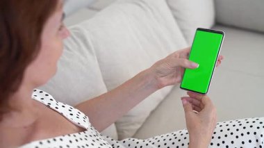 Kanepede rahat esmer kadın, yeşil ekranlı akıllı telefon, rahat ev atmosferi, dijital cihaz kullanımda, sosyal ilişki, modern yaşam, kablosuz bağlantı, çağdaş hayatın tadını çıkarma..