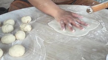 Huzurlu bir mutfakta, bir kadın ahşap bir oklava kullanarak hamuru yuvarlamaya odaklanır ve lezzetli gözleme için mükemmel bir temel oluşturur..