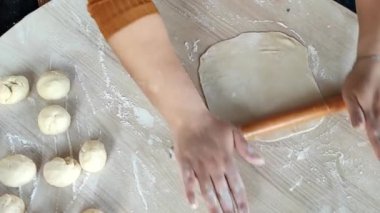 Sıcak bir mutfakta, yetenekli bir kadın ahşap bir oklava ile pürüzsüz hamuru ustalıkla çıkarıp leziz gözlüklere hazırlanıyor. Un, elleri özenle ve titizlikle çalışırken havada dans eder..