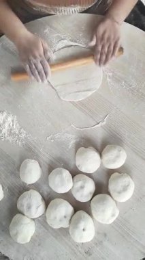 Sıcak bir mutfak ortamında, bir kadın yumuşak hamuru ahşap bir oklamayla ustalıkla yuvarlar..