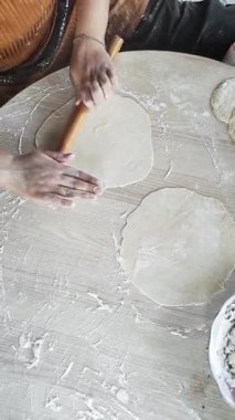 Sıcak bir mutfakta, bir kadın yumuşak hamuru ince daireler çizerek yuvarlarken odaklanır. Elleri bu geleneksel yemek pişirme anında lezzetli gozleme 'ye hazırlanmak için una bulanmış özenle çalışıyor..