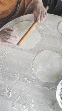 Eller hamuru un kaplı bir yüzeye nazikçe serer ve gözleme için ince mermiler oluşturur. Un çalışma alanının tozunu alıyor, geleneksel yemek yapma yöntemini vurguluyor. Evde bir mutfak sanatı anı yaşanıyor..