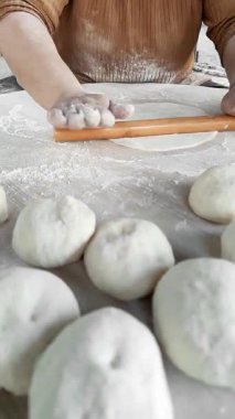 Elleri ustalıkla hamuru ahşap bir iğneyle çevirip ince daireler şeklinde şekillendiriyor. Un, yeni yapılmış gözlüklerin kokusu havayı doldururken yüzeyin tozunu alır ve sıcak bir mutfak ortamı yaratır..