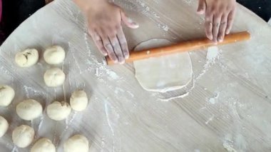 Sıcak bir mutfakta, bir kadın ahşap bir broşla hamuru zarifçe yuvarlar ve ustalıkla mükemmel bir daireye dönüştürür..