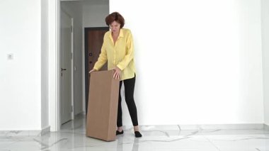 Parlak sarı bluzlu bir kadın yeni mobilyalarıyla dolu bir kutuyu açıyor. Yeni evinde toplanmaya hazırlanırken heyecan verici yeni taşınma projesi için her yeri dikkatlice kontrol ediyor..