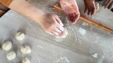 Sıcak bir mutfakta, bir kadın pide ekmek hamurunu ustalıkla hazırlar, elleri un içinde, çocuğu hevesle hamuru yuvarlamayı öğrenirken..