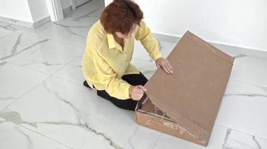 Bir kadın içinde yeni mobilya parçaları olan bir kutuyu açar, her bileşeni dikkatle inceler ve yeni evinde kusursuz bir montaj süreci için gereken her şeye sahip olduğundan emin olur..