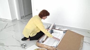 Bir kutu yeni mobilyayı heyecanla açan bir kadın parçaları montaj için dikkatlice inceliyor. Mekanını şık eklemeler ve düşünceli detaylarla değiştirmeye hazırlanıyor..