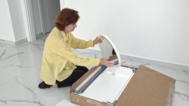 Bir kadın heyecanla mobilya parçalarıyla dolu bir kutuyu açıyor ve yaklaşan taşınma partisi için her parçayı dikkatlice kontrol ediyor. DY montaj yolculuğuna başlamak için gerekli şeyleri hazırlıyor..