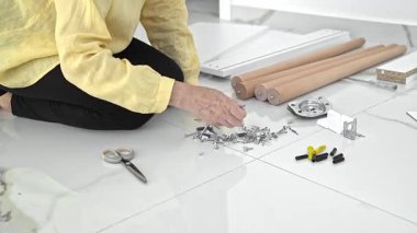 Yeni dairesindeki mobilyaların montajı için hazırlanırken vida ve aksesuarları dikkatlice sınıflandıran bir kadın..