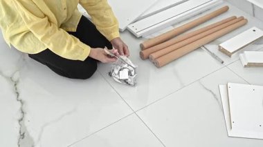 Mobilya montajı için parçaları ve aksesuarları dikkatlice kontrol eden bir kadın. Taşındıktan sonra yeni yaşam alanını hazırlarken heyecan havayı dolduruyor..