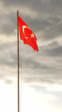 Beyaz hilal ay ve yıldızlı canlı bir kırmızı bayrak, Türkiye 'deki geniş ve bulutlu gökyüzüne karşı milli gururu sembolize eden bir bayrak direğine asılıyor..
