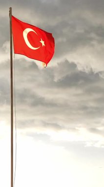 Beyaz bir yıldız ve hilal içeren çarpıcı bir Türk bayrağı bayrak direğinde zarafetle açılıyor. Arkaplan dalgalı bulutlarla doludur, gurur ve kimlik atmosferi yaratır..