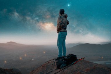 Sırt çantasının silueti tepenin üstünde, Samanyolu 'nu şehrin üzerinde seyrediyor.