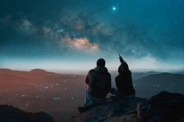 一对夫妇坐在山顶上凝视着城市上空的星星的轮廓 — 图库照片