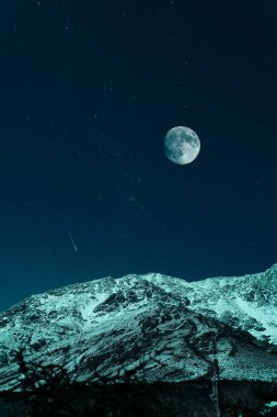 Dolunay altında gece karlı dağ ve arka planda yıldızlı