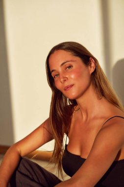 Kafasında portre olan beyaz bir kadın yerde oturmuş kendine güvenerek gülümsüyor.