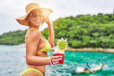 Sahilde elinde meyve suyu tutan bikinili genç bir kadın. 