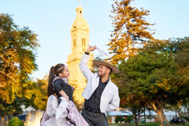 waist up portrait young adult latin american couple dancing cueca national dance with huaso dress in the city square of La Serena clipart