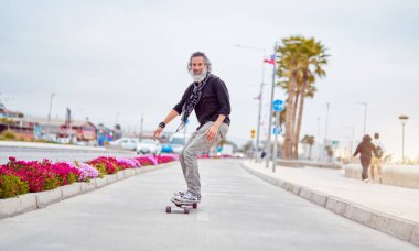 Olgun beyaz sakallı adam bisiklet yolunda kayıyor ve eğleniyor.