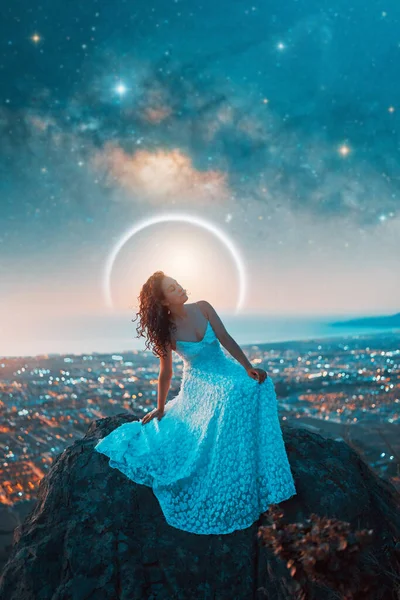 portrait beauty fantasy woman with white dress on a rock and stars and milky way over the city in the background