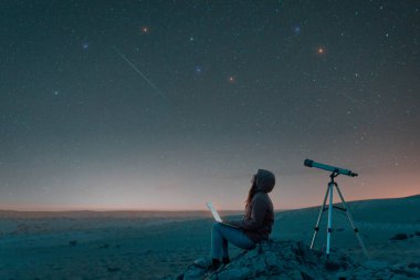  woman sitting in the desert with a laptop next to a telescope at night watching the starry sky, astronomy and stargazing concep clipart