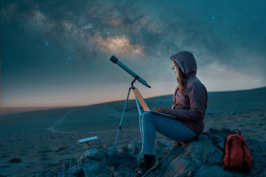 Geceleri çölde dizüstü bilgisayarı olan dijital göçebe bir kadın Samanyolu 'nun yanında oturuyor.