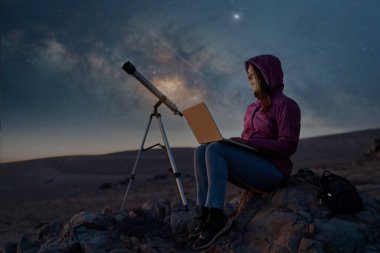 woman sitting in the desert with a laptop next to a telescope at night under the stars and milky way, astronomy and stargazing concept  clipart