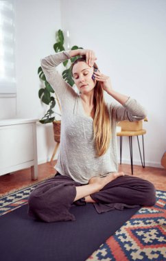 Güzel beyaz bir kadın şakaklarına ve yüzüne elle masaj yapıyor. Kuvars masaj aleti, yüz yogası ve yaşlanmayı önlüyor.