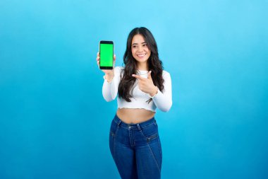 Stüdyoda cep telefonu ekranını gösteren gülümseyen Latin kadının portresi.