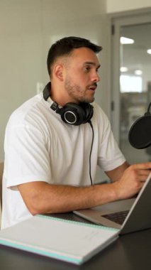 Beyaz tişörtlü bir adam stüdyoda ses yayını kaydediyordu. Laptop kullanıyordu ve konuğuyla konuşuyordu. 