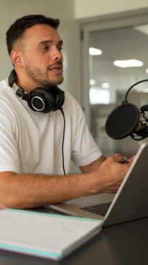 Beyaz tişörtlü bir adam stüdyoda ses yayını kaydediyordu. Laptop kullanıyordu ve konuğuyla konuşuyordu. 