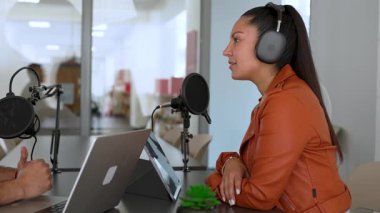 İki radyo sunucusu bir stüdyoda canlı yayın sırasında sohbet ediyorlar. Masada oturan kulaklık takan erkek ve kadın kayıt için dizüstü bilgisayar ve tablet bilgisayar kullanıyor. 