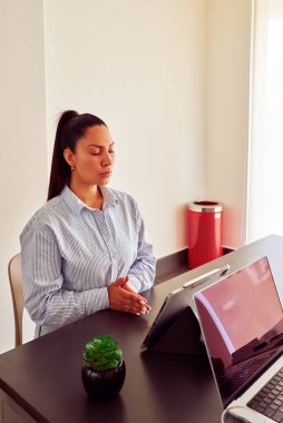 İş kadını kapalı gözlerle meditasyon yapıyor, huzuru buluyor ve modern ofisinde odaklanıyor, zihinsel refahı ve iş hayatı dengesini destekliyor.