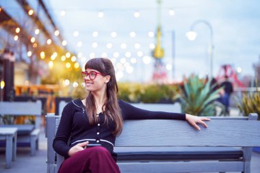 Güzel bir portre gülümseyen beyaz bir kadın şehir sokaklarında bir bankta oturuyor.