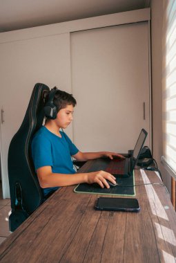 Çocuk kulaklık takıyor, bilgisayar ve fare kullanıyor, video oyunları oynuyor, oyun sandalyesinde oturuyor.