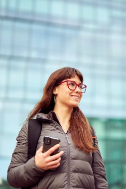 İspanyol bir banliyö kadınının portresi cep telefonuyla modern bir bina geçmişi, şehir hayatı konseptini karşılaştırıyor.