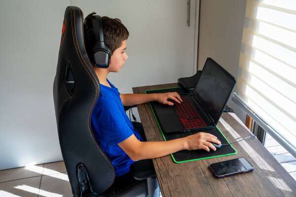 Gamer boy playing video games using a laptop and wearing headphones in a gaming chair