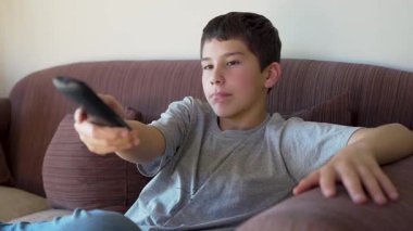 Gençler televizyon izliyor, uzaktan kumandayla kanal değiştiriyor.