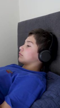 Kulaklık takan Latin çocuk yatakta video oyunları oynamaktan hoşlanıyor.