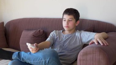 Çocuk televizyon izliyor, uzaktan kumandayla kanal değiştiriyor.