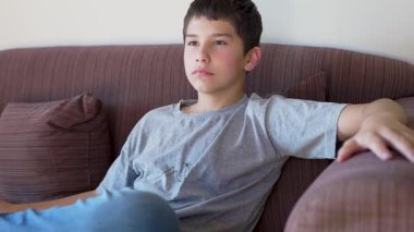 çocuk evdeki kanepede oturup televizyon izliyor.