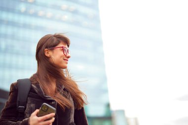 Arka planda sırt çantası ve binası olan Kafkasyalı genç iş kadını portresi.