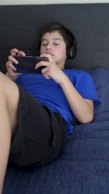 Kulaklık takan genç çocuk yatakta video oyunları oynamaktan hoşlanıyor