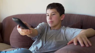 Gençler televizyon izliyor, uzaktan kumandayla kanal değiştiriyor.