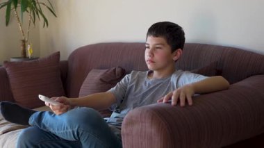 Çocuk televizyon izliyor, uzaktan kumandayla kanal değiştiriyor.