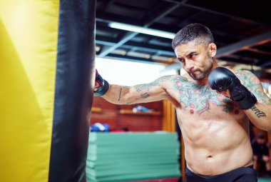 Erkek boksör boks salonunda ağır bir torba üzerinde yumruklarını çalışıyor.